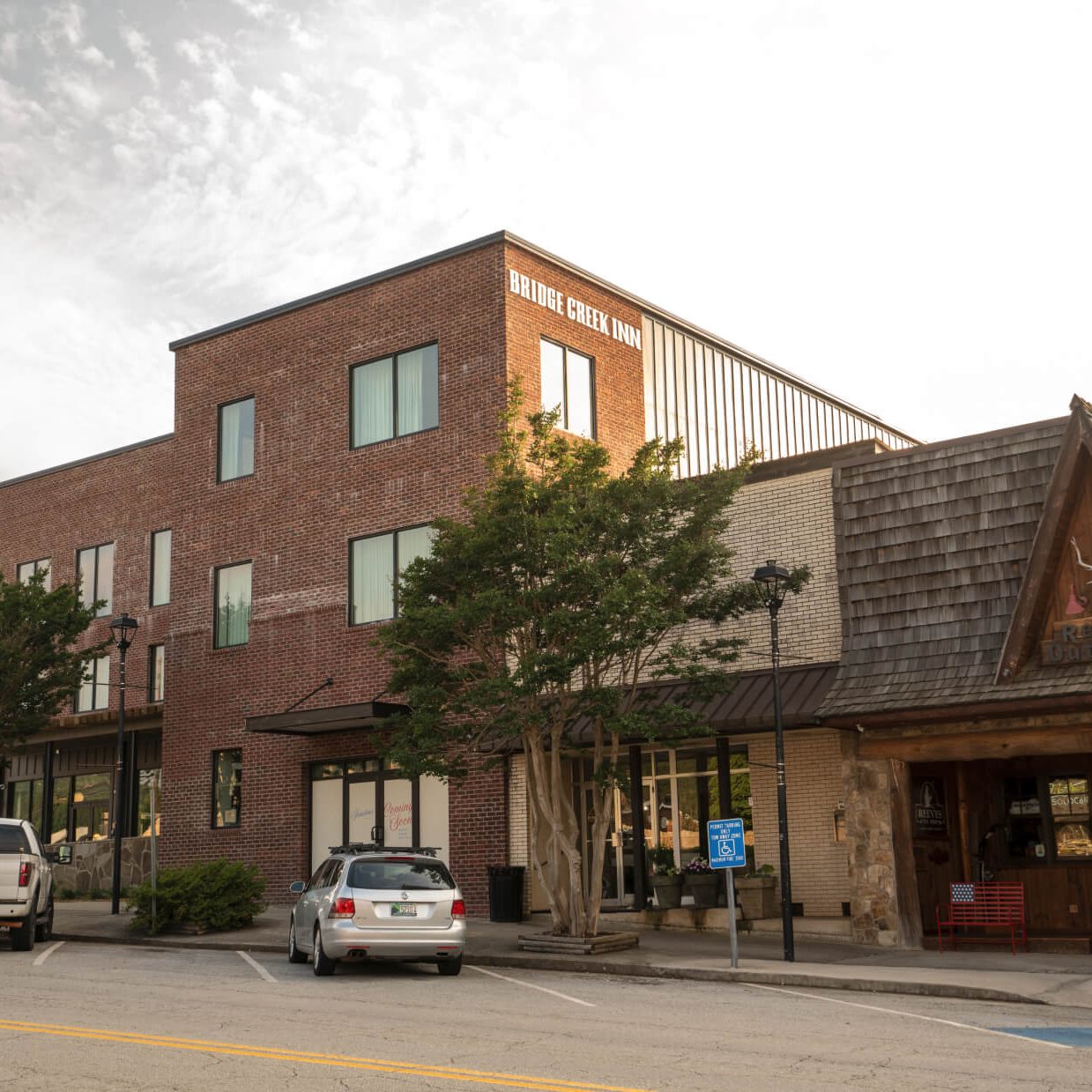 Brick hotel building with a 'Bridge Creek Inn' sign, two-story windows, and trees in front; parked cars along the street. - Clayton, GA
