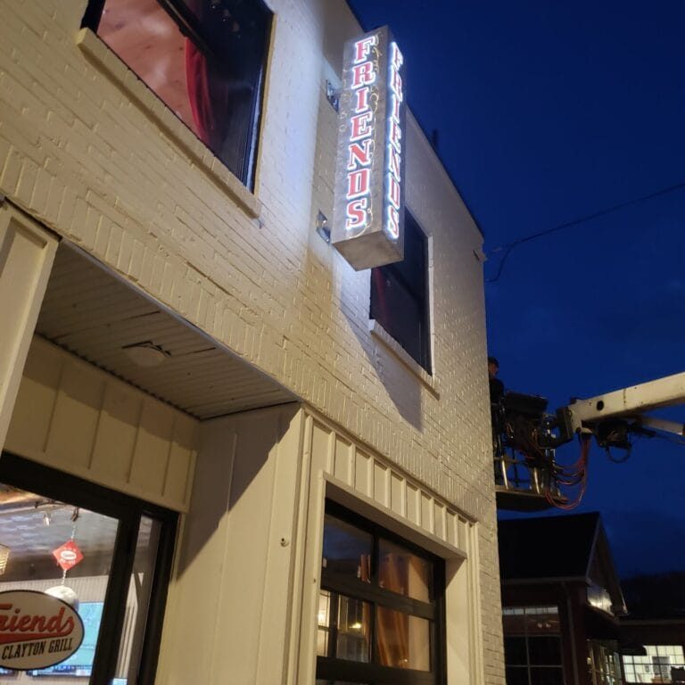 Nighttime exterior of a white brick restaurant with a vertical neon sign reading 'FRIENDS' on the corner. - Clayton, GA