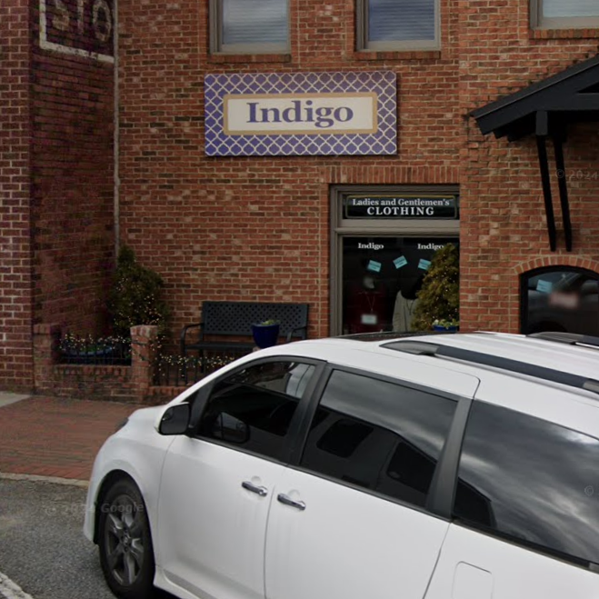 White minivan parked in front of a brick storefront with an Indigo sign above and a clothing shop window in view. - Clayton, GA