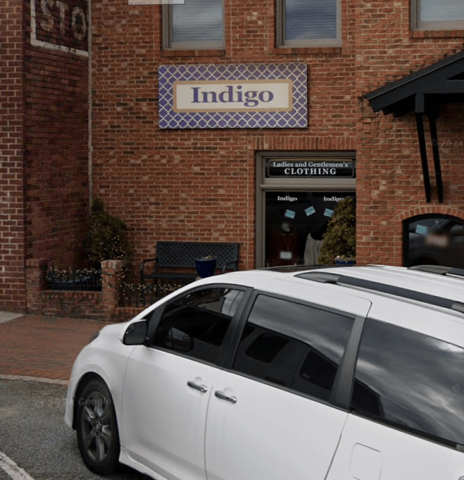 Indigo - Visit Clayton, GA White minivan parked in front of a brick storefront with an Indigo sign above and a clothing shop window in view. - Clayton, GA