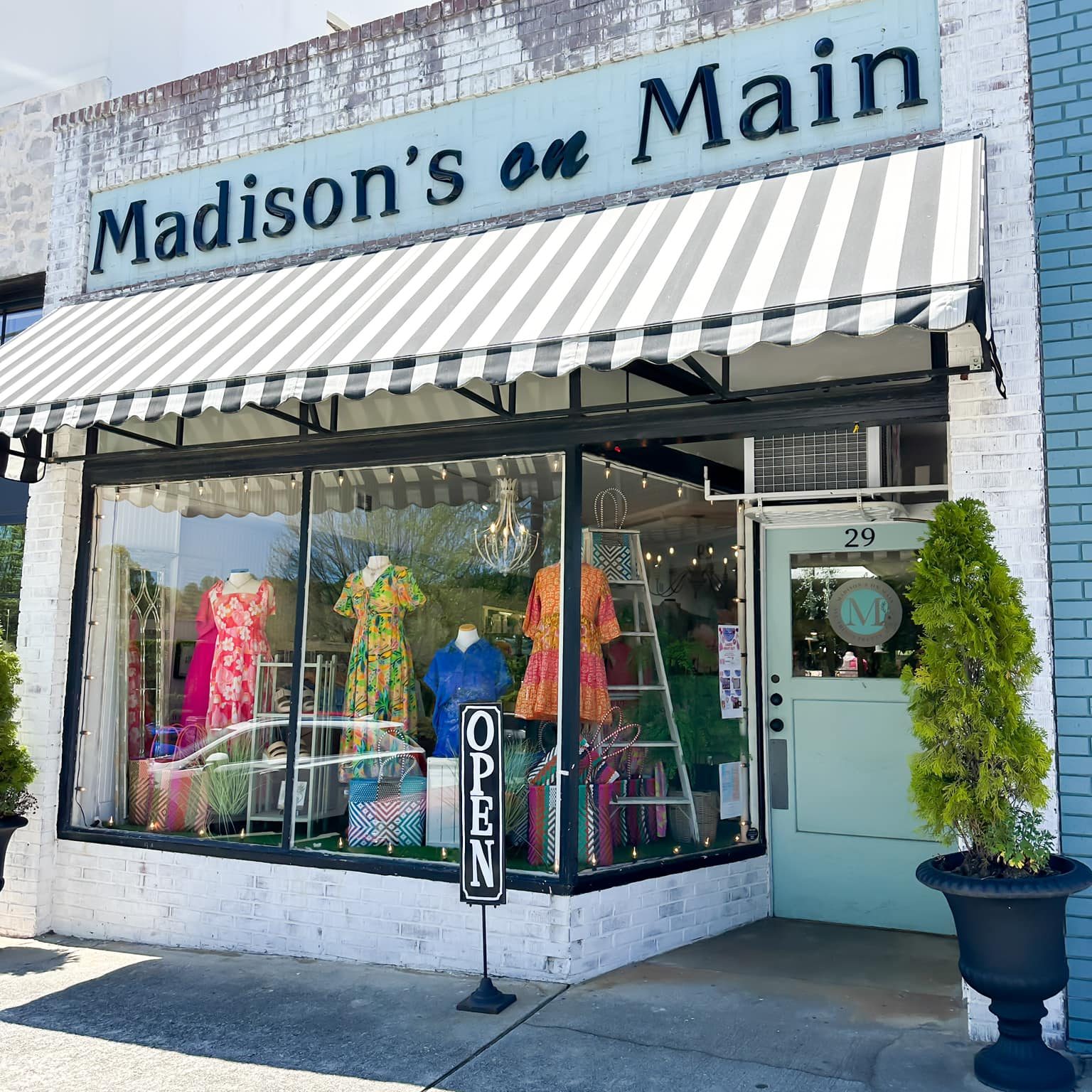 Storefront clothing shop with a black-and-white striped awning and colorful dresses in the window display. - Clayton, GA