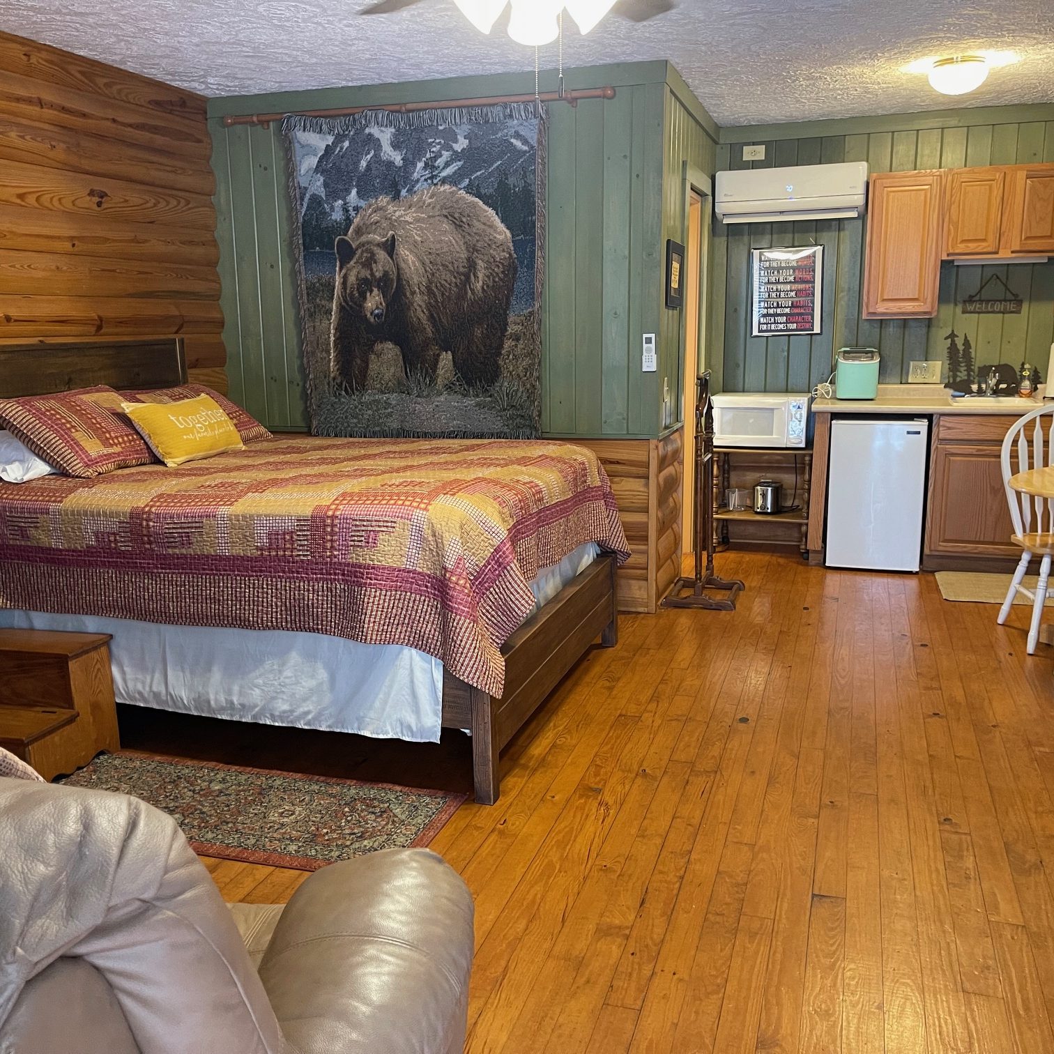Rustic cabin bedroom with log walls, a queen bed, patchwork quilt, and a large bear tapestry on a green paneled wall. - Clayton, GA