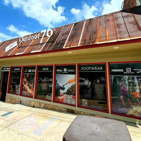 Front of an Outdoor 70 store with large window displays advertising gear and footwear, stone facade, and a small American flag on the left. - Clayton, GA