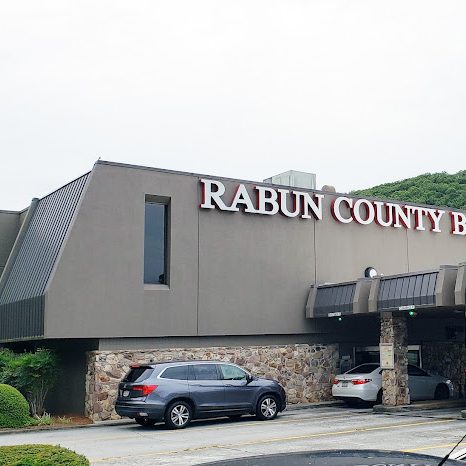 Exterior view of Rabun County Bank building with a stone entrance and parked cars under a covered drive-through area - Clayton, GA