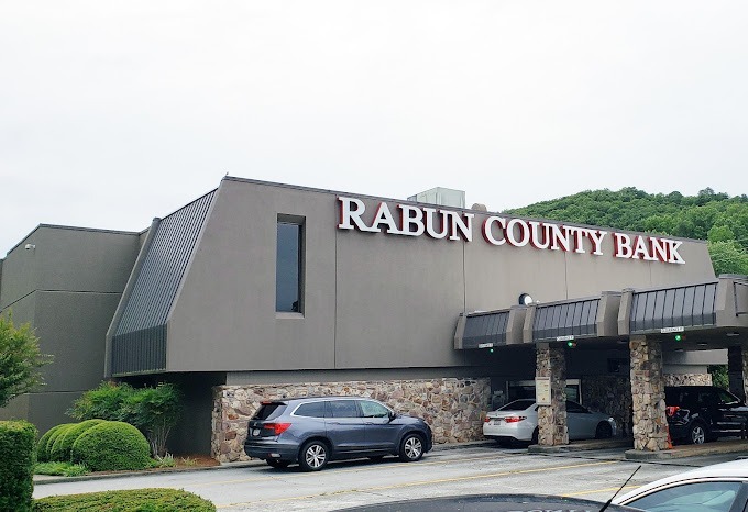Rabun County Bank Exterior view of Rabun County Bank building with a stone entrance and parked cars under a covered drive-through area - Clayton, GA