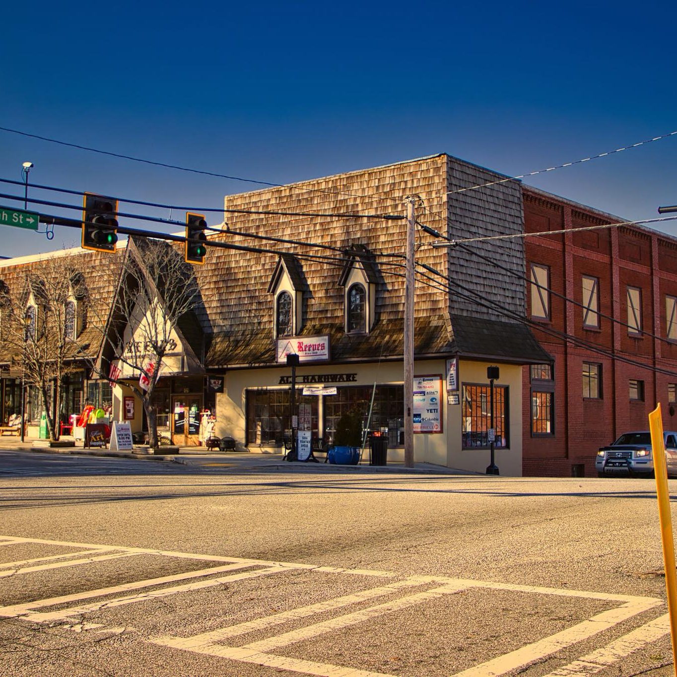 Intersection at N Main St and W Savannah St with brick buildings, traffic lights, and a yellow street pole in the foreground - Clayton, GA