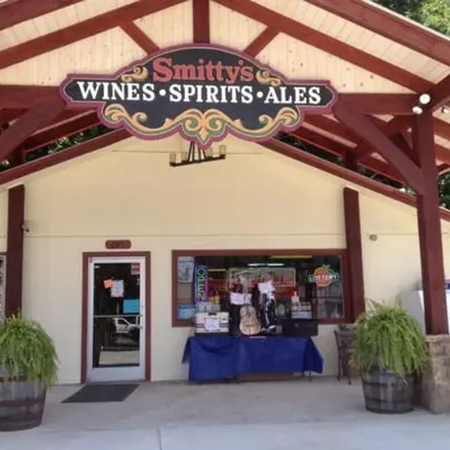 Storefront of Smitty's Wines Spirits Ales, with a blue table of items by the entrance under a red wooden awning. - Clayton, GA