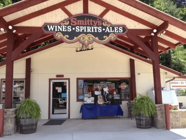 Smitty’s Spirits Storefront of Smitty's Wines Spirits Ales, with a blue table of items by the entrance under a red wooden awning. - Clayton, GA