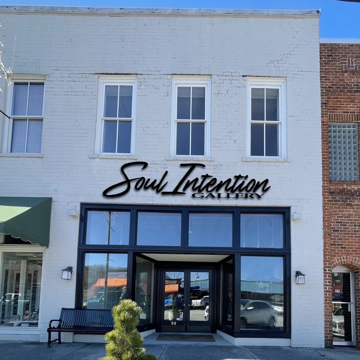 White brick storefront with three second-floor windows and a black-framed glass entry, displaying 'Soul Intention Gallery' above the door. - Clayton, GA