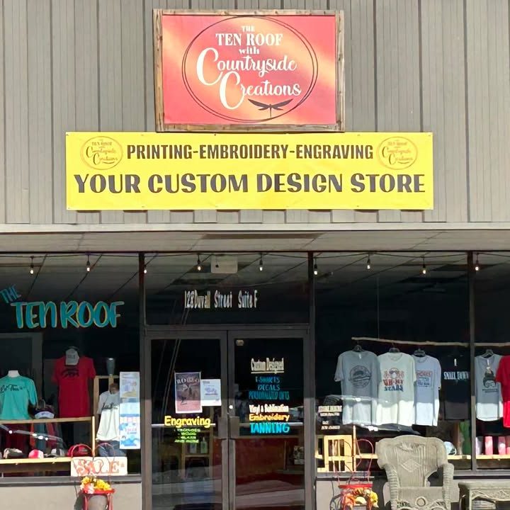 Front of a custom design shop with a bright yellow sign reading 'Your Custom Design Store' and t-shirt displays in the window. - Clayton, GA