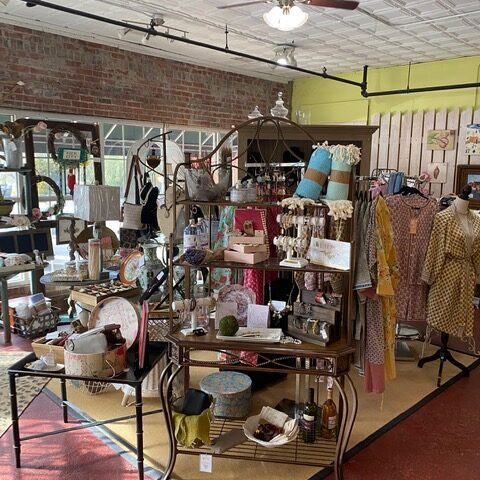 Inside a vintage boutique with display shelves of purses, hats, and accessories, wooden racks of clothing along exposed brick walls and ceiling fans overhead. - Clayton, GA