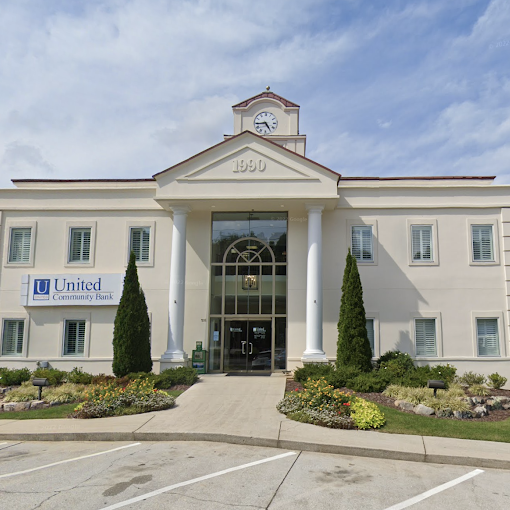 Front view of a beige bank building with a clock tower and two tall columns at the entrance, landscaping in front and a United Community Bank sign on the left. - Clayton, GA