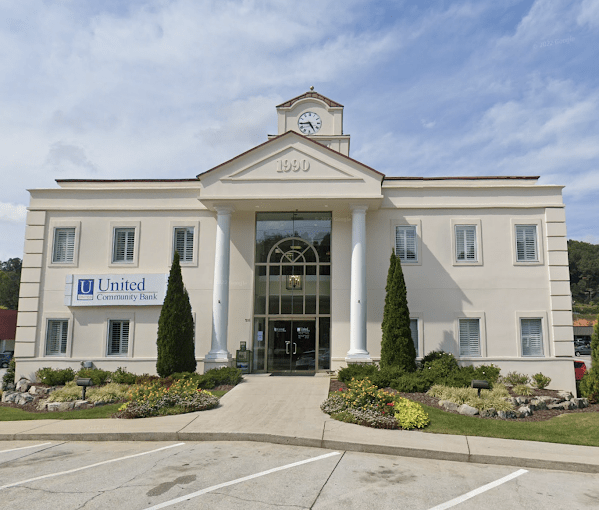 United Community Bank Front view of a beige bank building with a clock tower and two tall columns at the entrance, landscaping in front and a United Community Bank sign on the left. - Clayton, GA