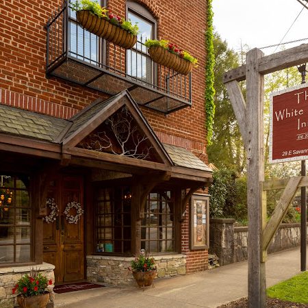 Brick inn with wooden entryway and balconies, hanging flower baskets, and a sign reading 'The White Birch Inn' on a wooden post by the sidewalk. - Clayton, GA