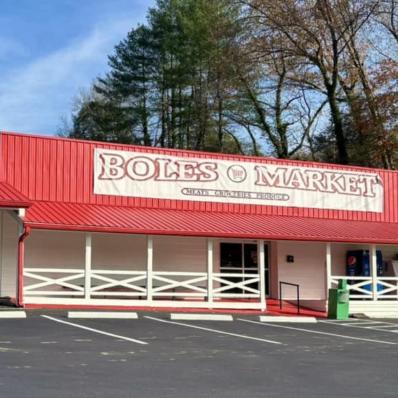 Front view of Boles Market, a single-story store with a red roof and white exterior, parking lot in foreground. - Clayton, GA
