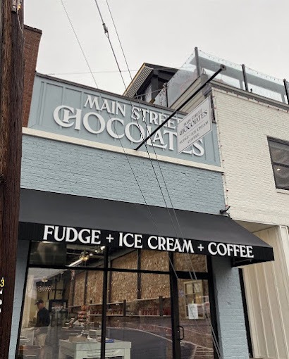 Main Street Chocolates - Visit Clayton, GA Storefront with a light blue facade and a sign that reads 'Main Street Goods', plus a black awning that says 'Fudge + Ice Cream + Coffee' - Clayton, GA