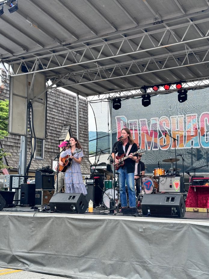Female guitarist and vocalist performing on an outdoor stage with a drummer in the background. - Clayton, GA