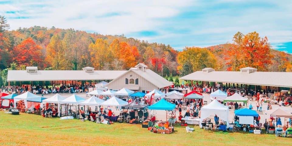 Sassafras Artisan Market Outdoor autumn market with numerous white tents and vendors on a grassy field, colorful fall trees in the background. - Clayton, GA