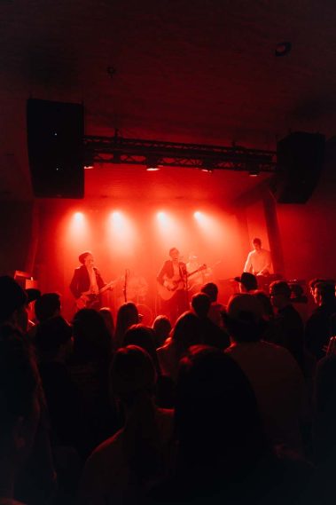 Band performing on a red-lit stage with a crowd in the foreground. - Clayton, GA
