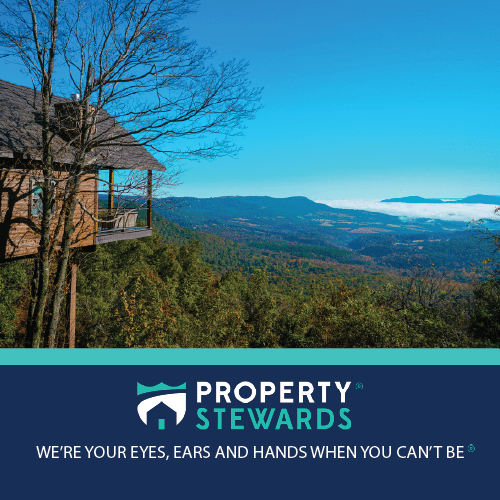 Wood cabin balcony perched on a hillside with forest and distant blue mountains under a bright sky; Property Stewards branding at the bottom. - Clayton, GA