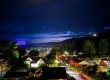 Nighttime hillside town with a blue illuminated sign reading 'AMERICA 50' on the left; cars and houses lit below. - Clayton, GA