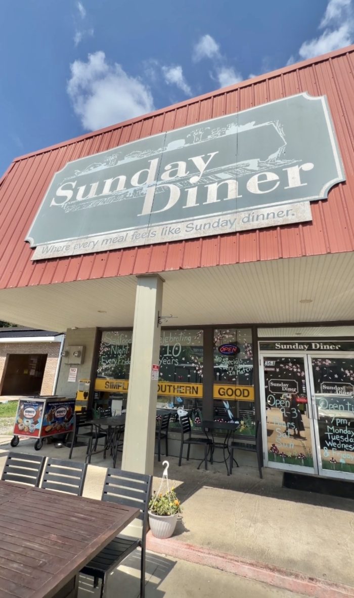 Front of Sunday Diner with a large gray sign reading 'Sunday Diner' above outdoor seating. - Clayton, GA