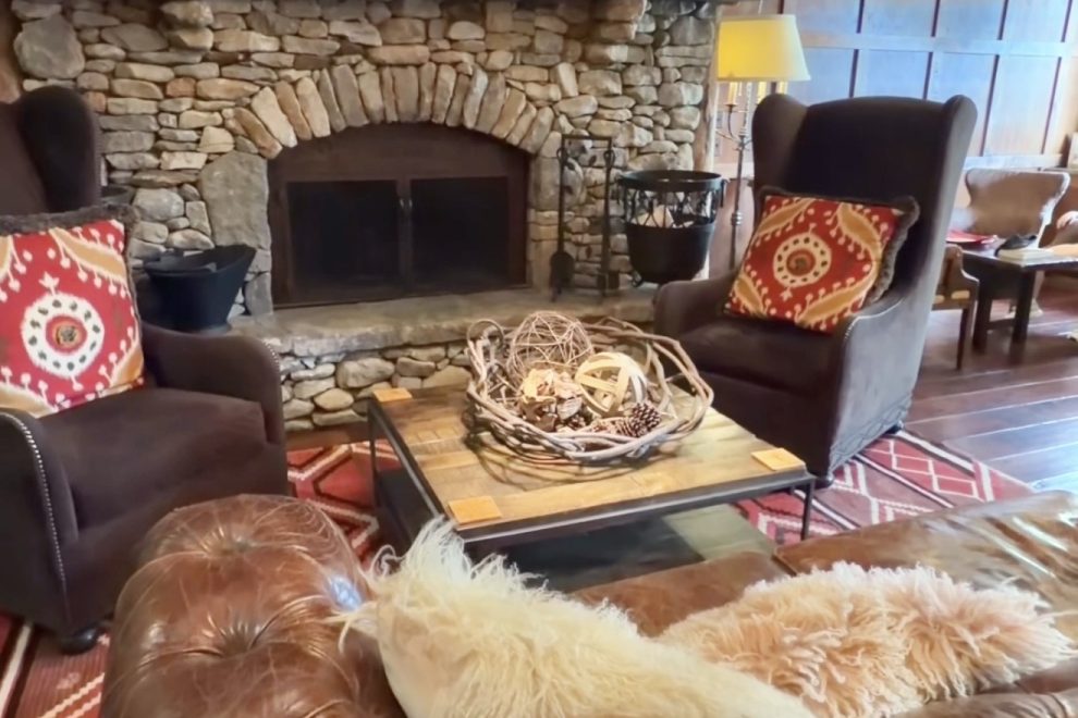Cozy living room with a stone fireplace, leather sofa, and colorful hanging lanterns above a wooden coffee table.