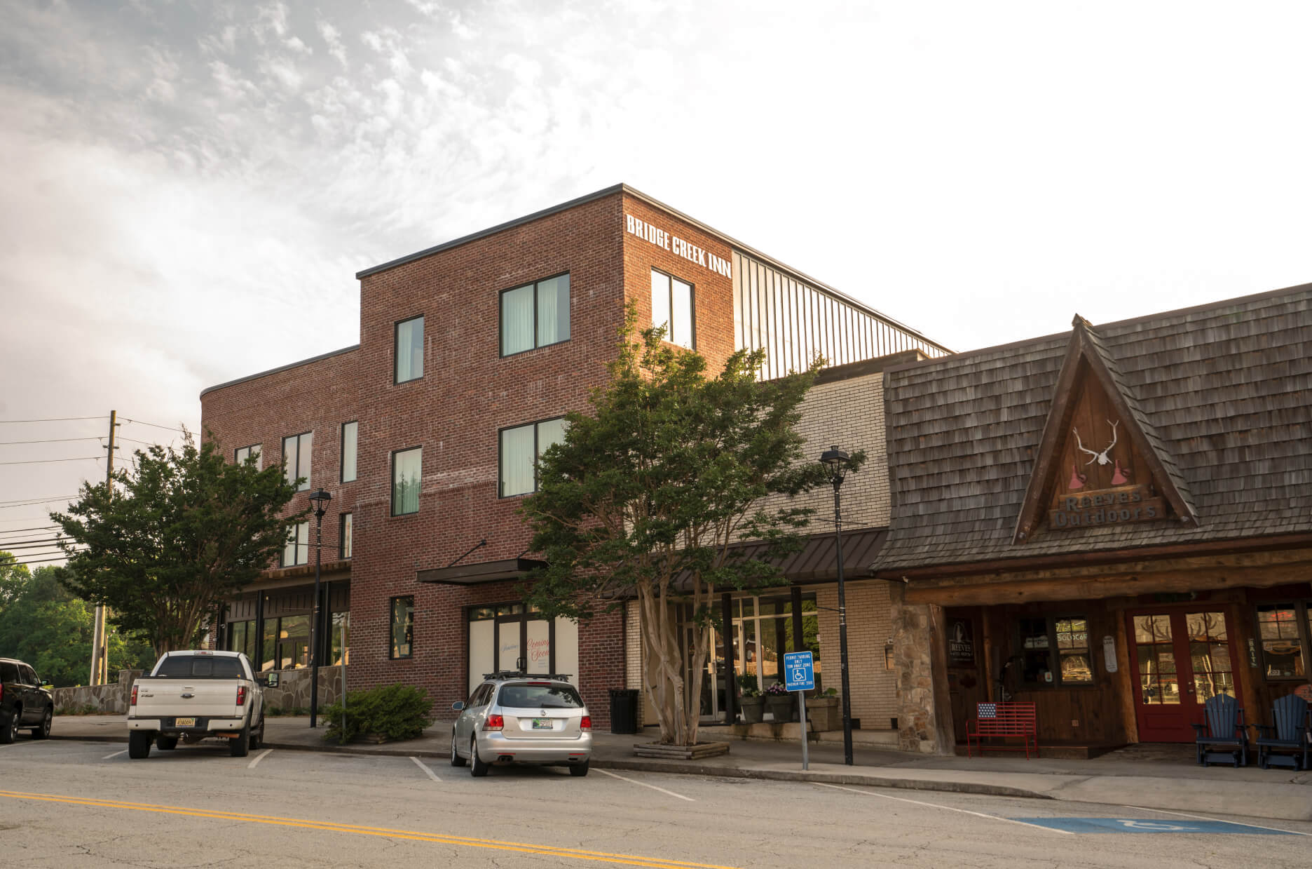 Brick hotel building with a 'Bridge Creek Inn' sign, two-story windows, and trees in front; parked cars along the street. - Clayton, GA