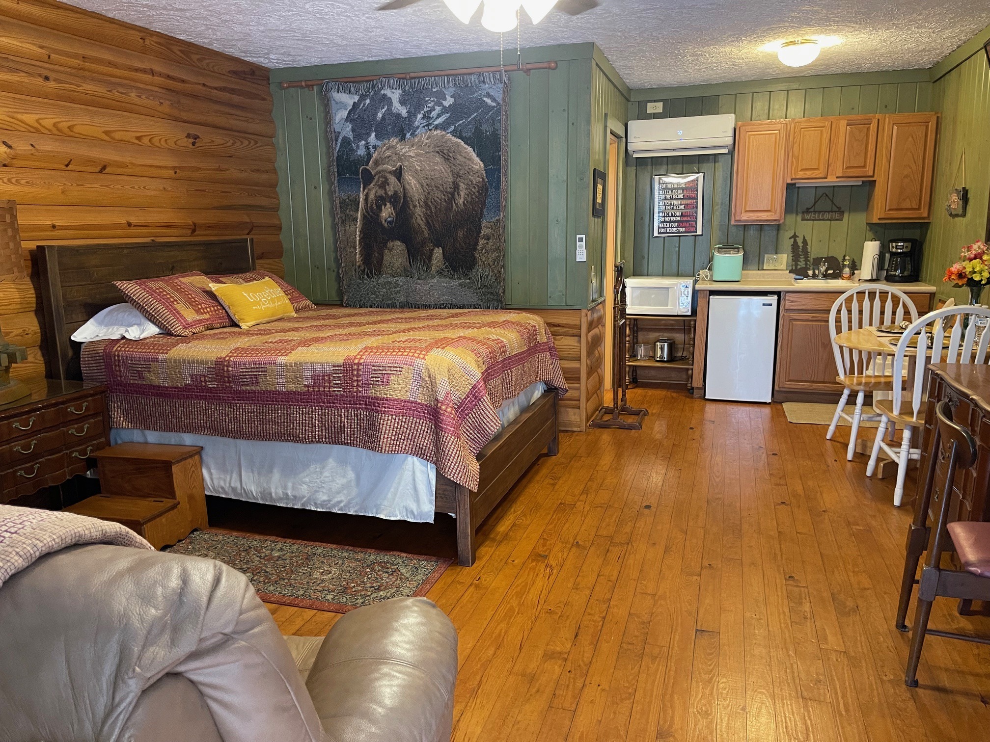 Rustic cabin bedroom with log walls, a queen bed, patchwork quilt, and a large bear tapestry on a green paneled wall. - Clayton, GA