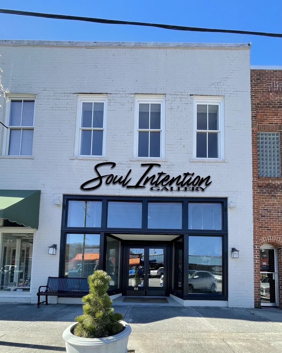 White brick storefront with three second-floor windows and a black-framed glass entry, displaying 'Soul Intention Gallery' above the door. - Clayton, GA