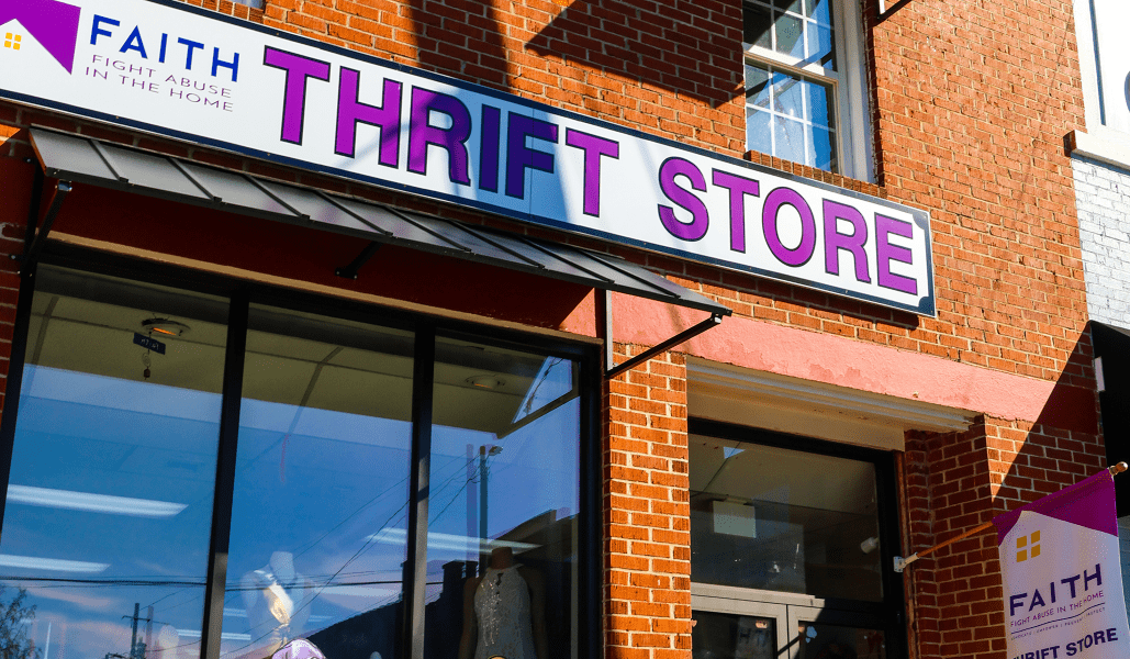 Storefront with a bold 'THRIFT STORE' sign on a red brick building and a Faith anti-abuse banner above. - Clayton, GA