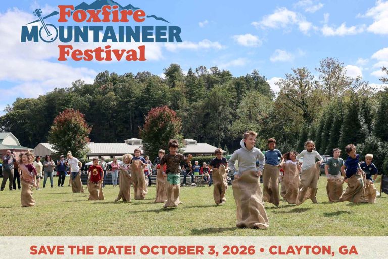 Promotional banner for Foxfire Mountaineer Festival with people in a sack race on a green field; date is October 3, 2026 in Clayton, GA.
