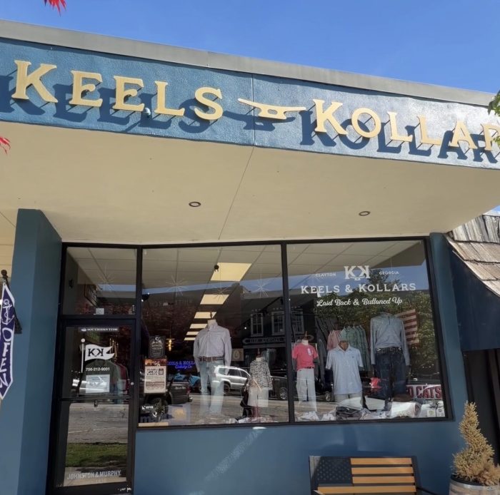 Storefront of Keels & Kollars clothing shop with large sign, glass display window showing mannequined outfits and a patriotic display outside in Clayton, Georgia.