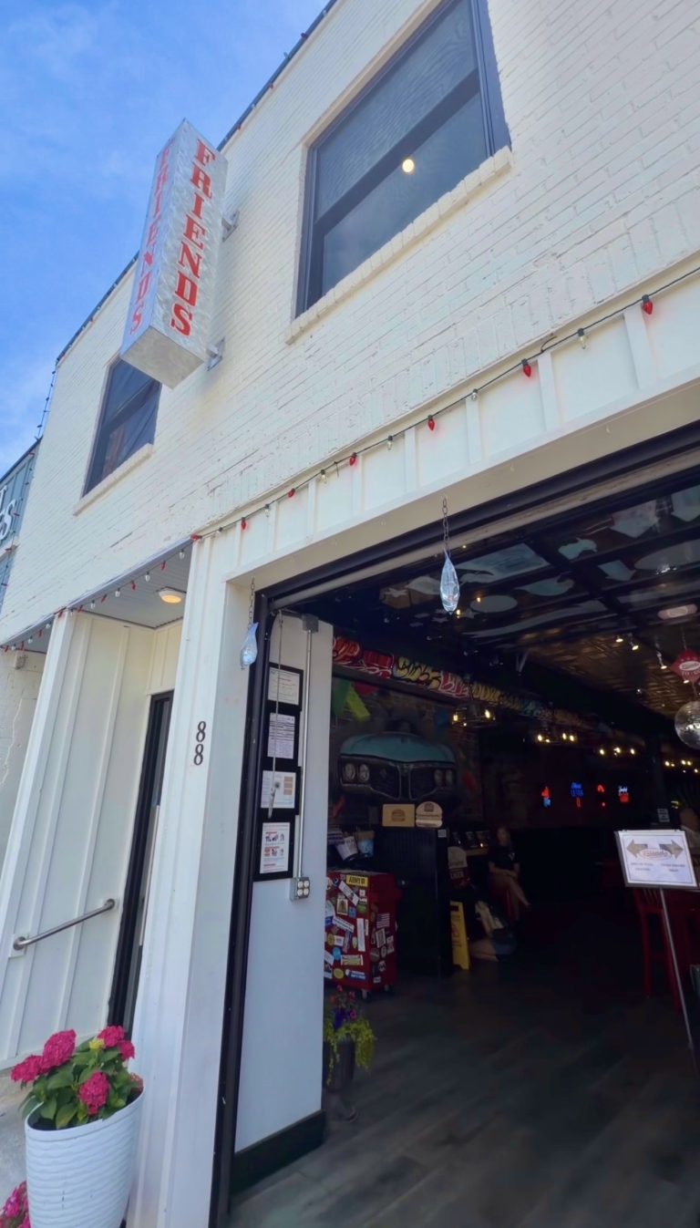 Open storefront with a vertical 'FRIENDS' sign on white brick, large garage-style door revealing a vintage car inside and memorabilia.
