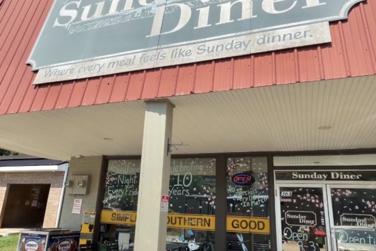 Front of Sunday Diner with a large gray sign reading 'Sunday Diner' above outdoor seating.