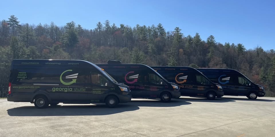 Georgia Shuttle Inc. - Visit Clayton, GA Three dark Georgia Shuttle vans lined up on a paved lot with trees in the background. - Clayton, GA