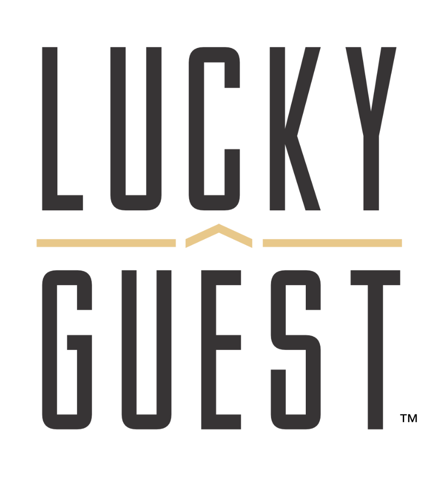 Lucky Guest - Visit Clayton, GA Lucky Guest logo: tall black letters spell 'LUCKY' above 'GUEST' with a beige chevron between and beige lines on either side. - Clayton, GA