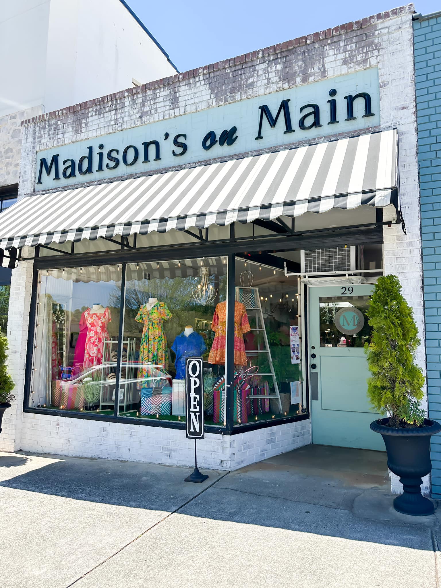 Madison's On Main - Visit Clayton, GA Storefront clothing shop with a black-and-white striped awning and colorful dresses in the window display. - Clayton, GA