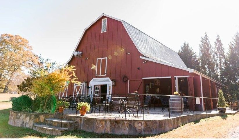 Tiger Mountain Vineyards The Vineyard Café at Red Barn - Visit Clayton, GA Red barn with white trim and metal roof, outdoor seating on a raised stone patio. - Clayton, GA