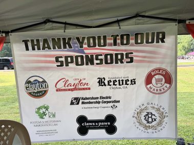 Outdoor sponsor banner reading 'Thank you to our sponsors' under a tent with multiple logos visible in a park setting.