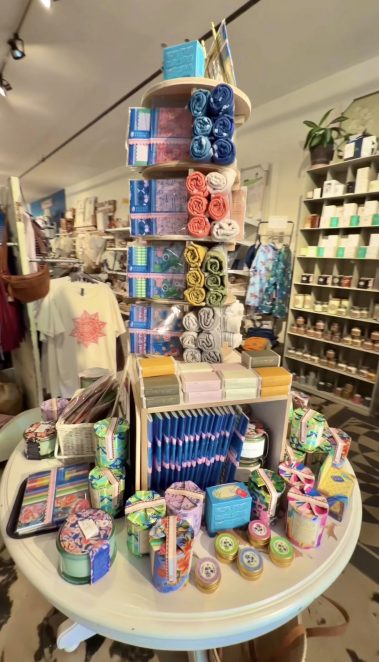 Colorful gift display in a shop: stacked circular shelves with rolled towels in blue, teal, pink, and orange, plus boxed soaps and colorful packaging on a rotating tower.