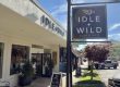 Idle + Wild Home & Gifts storefront with a hanging sign against a bright blue sky on a sunny day.