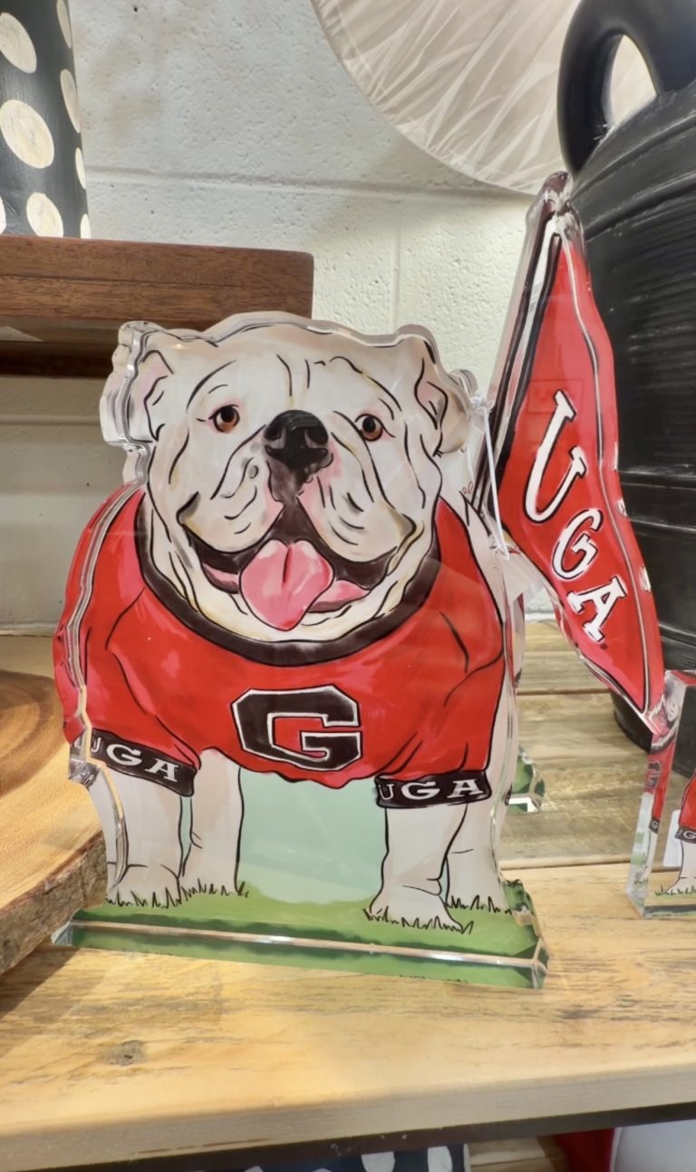 Colorful bulldog cutout wearing a red Georgia Bulldogs jersey with a big 'G' on the chest, tongue out, standing on a wooden shelf.