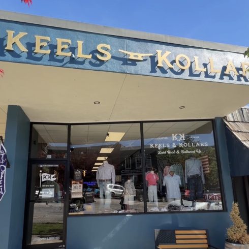 Storefront of Keels & Kollars clothing shop with large sign, glass display window showing mannequined outfits and a patriotic display outside in Clayton, Georgia.