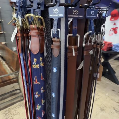 Display of assorted leather belts on a rotating rack in browns and blues with blue tags reading Southern Tide.