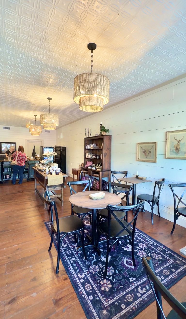 Cozy cafe interior with round wooden tables, black chairs, and woven wicker pendant lights hanging from a patterned ceiling.