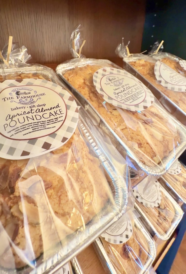 Apricot almond poundcake loaves in clear plastic wrap with round checkered labels from The Farmhouse bakery gift shop (displayed on a shelf).
