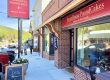 Exterior view of FarmHouse PoundCakes bakery on a sunny street, brick storefront, red sign, and open doorway with a chalkboard menu outside.