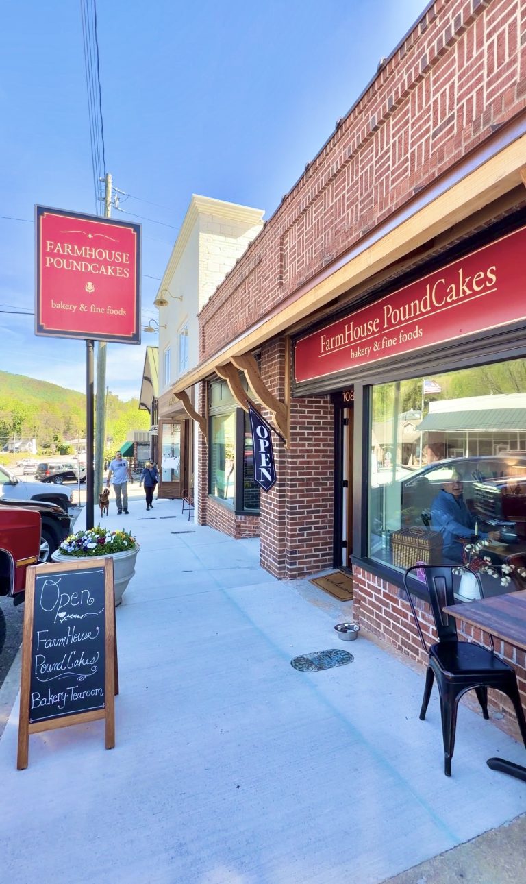 Exterior view of FarmHouse PoundCakes bakery on a sunny street, brick storefront, red sign, and open doorway with a chalkboard menu outside.