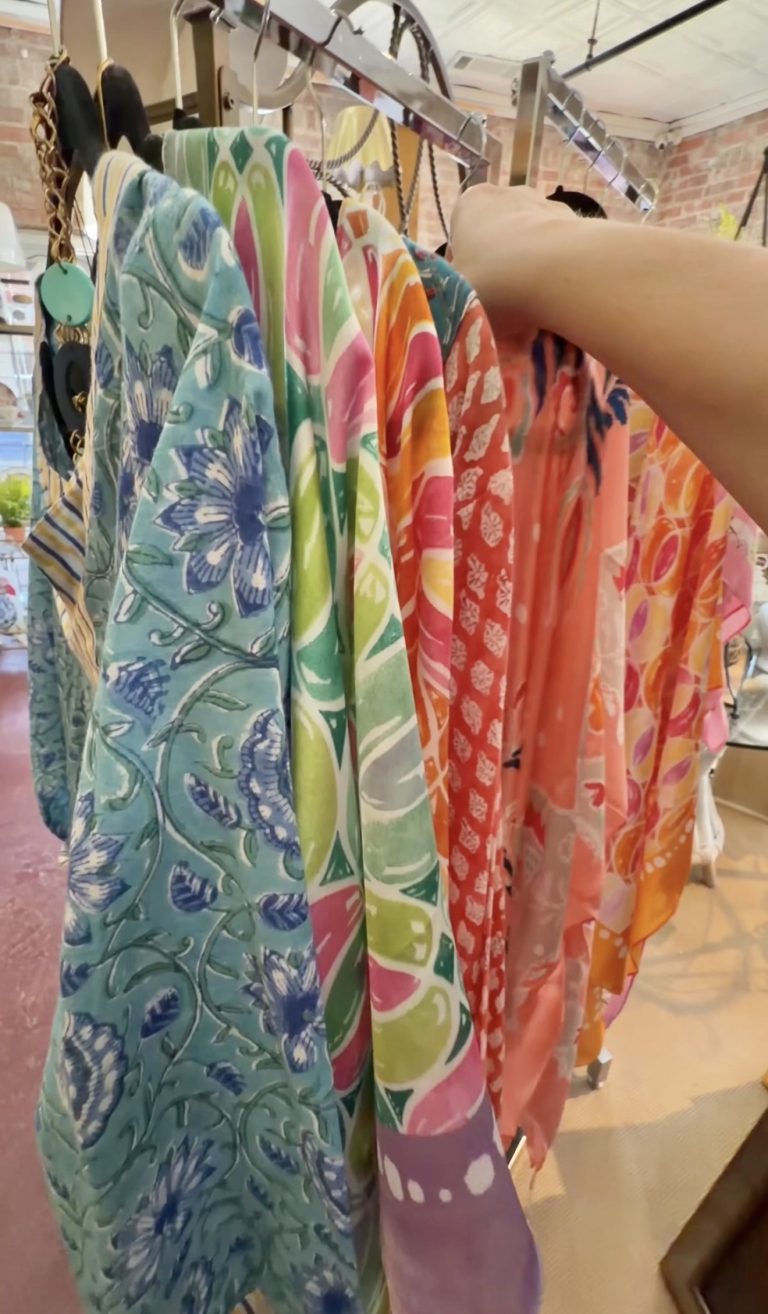 Rack of colorful patterned scarves hanging on a clothes rail in a store setting.